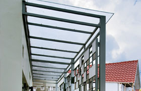 Pérgola adosada de acero con cubierta de vidrio sobre el acceso de una casa