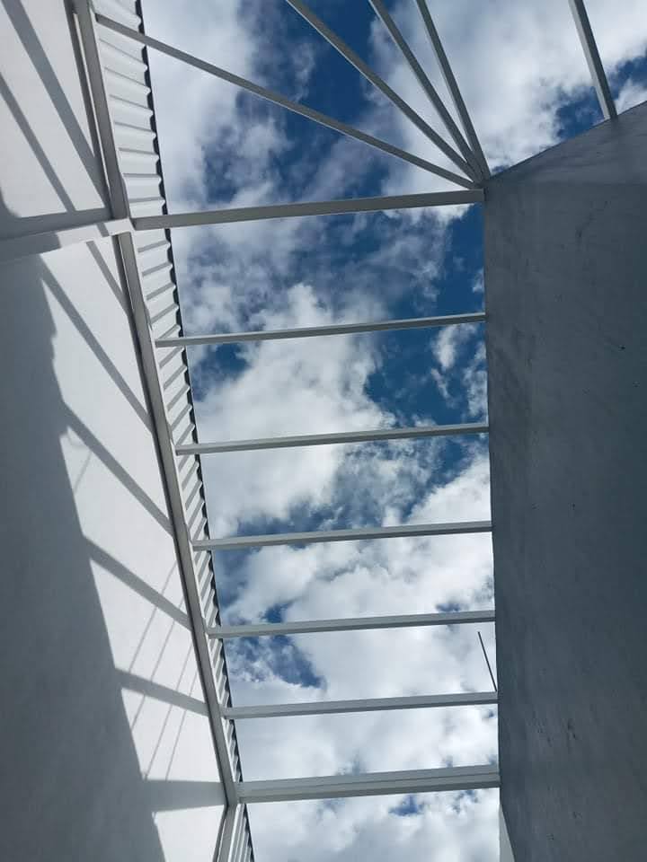 Vista desde abajo de una pérgola de acero, mirando hacia el cielo entre los travesaños de la estructura