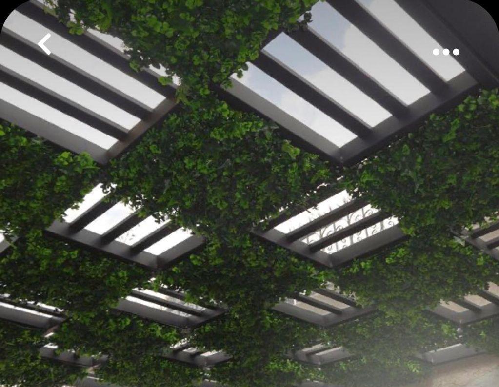 Pérgola de acero tipo tablero con barrotes, plantas colgantes y pasto sintético